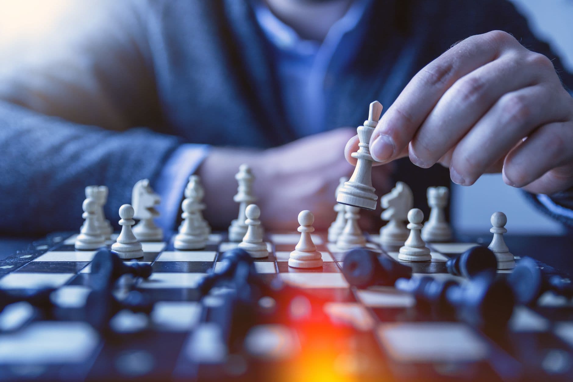 Close-up of a hand making a strategic chess move on a board, emphasizing thought and planning.