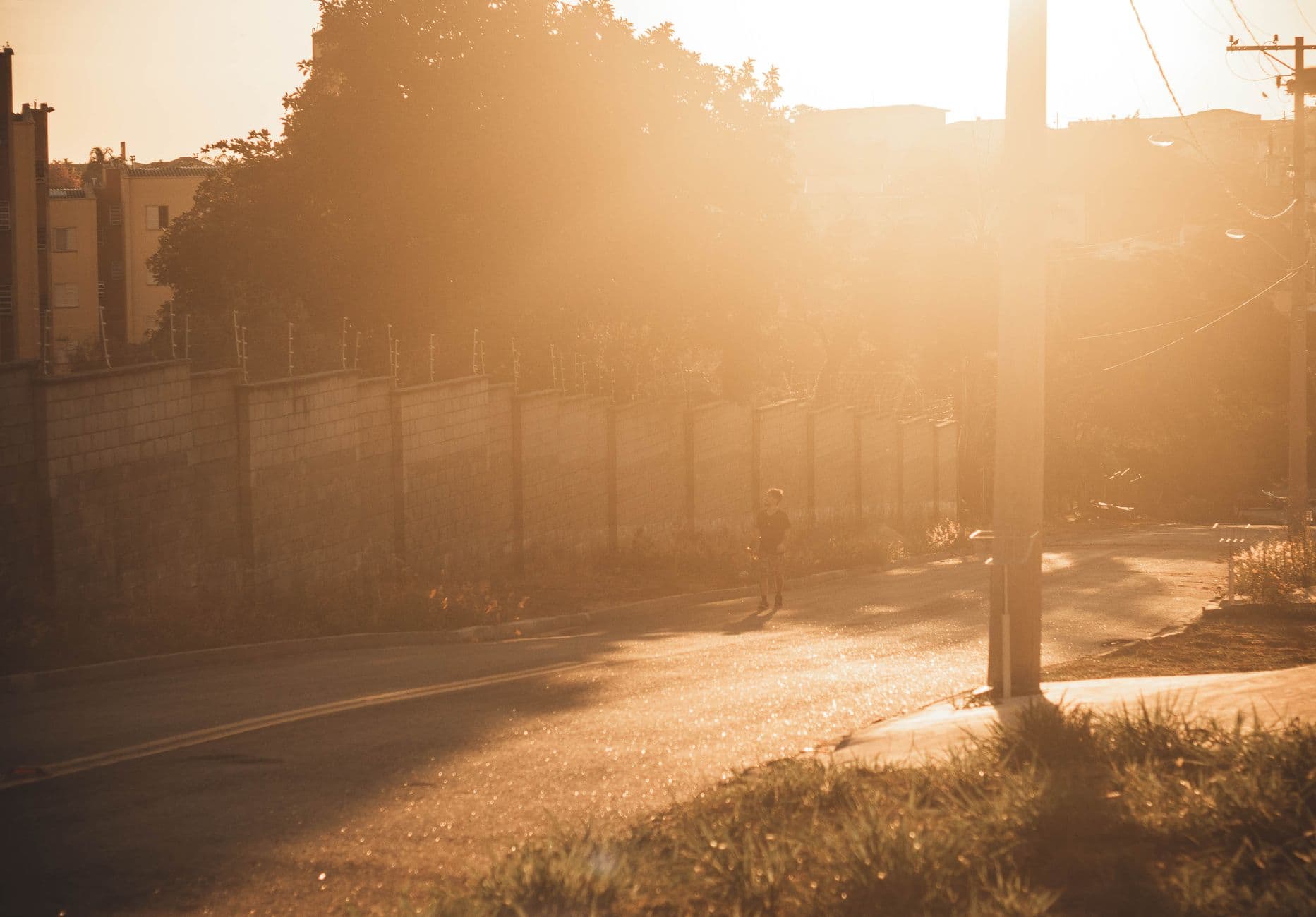 A person walking down a sunny road during golden hour, casting long shadows in the warm glow.