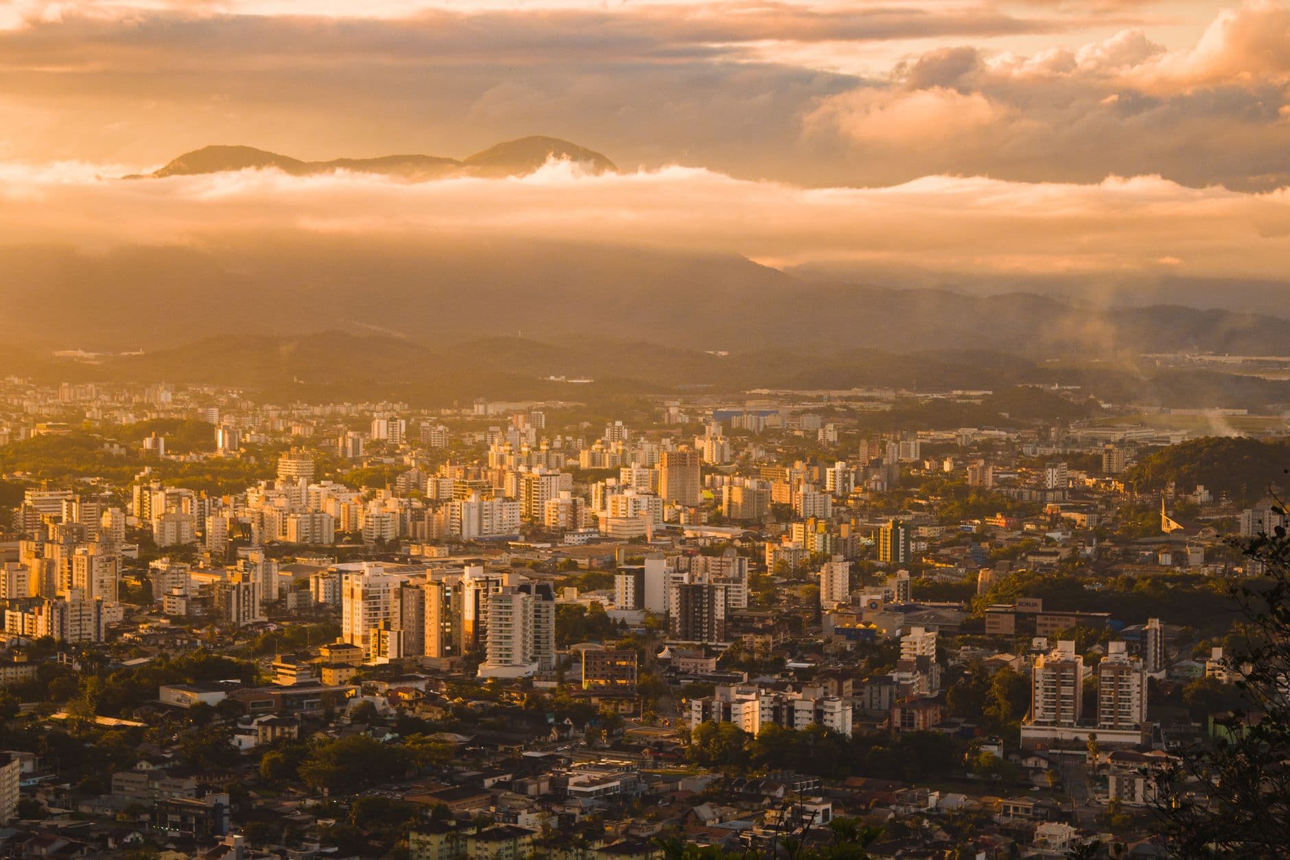 An aerial view of a vibrant cityscape under a warm sunset, highlighting urban architecture and distant mountains.