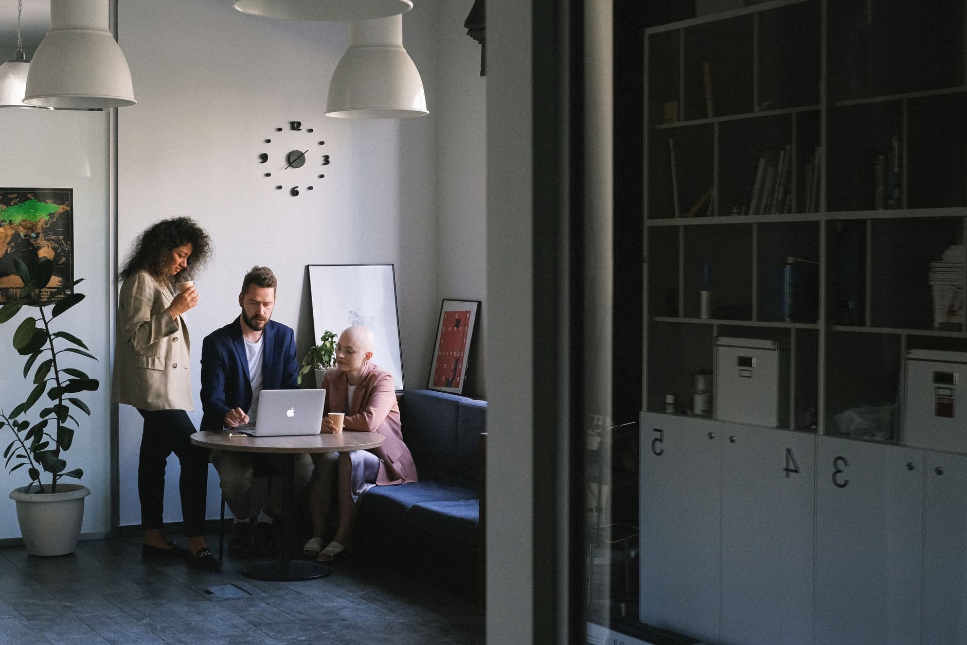 Multiethnic serious businesspeople working while browsing netbook at table in contemporary office with shelves