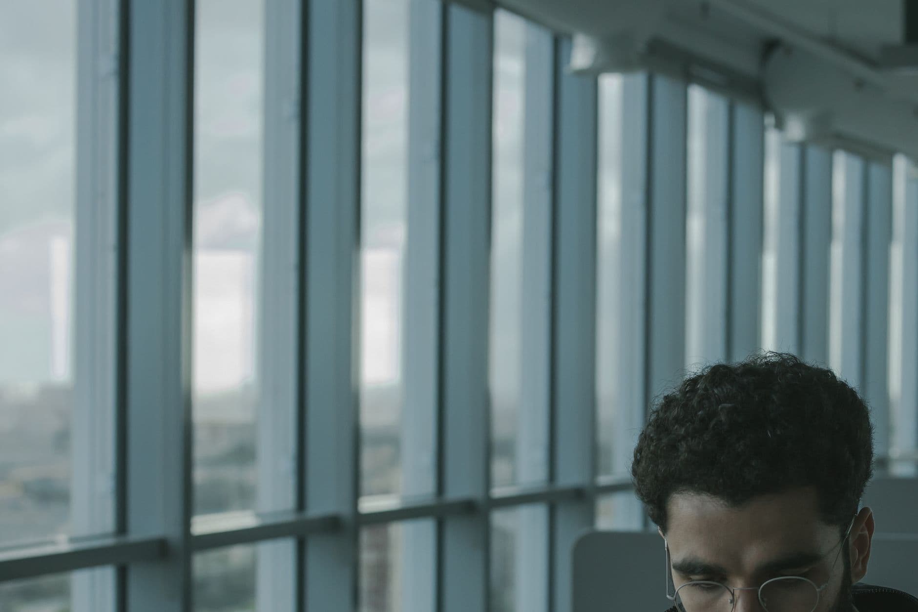 Man seated in airport lounge wearing glasses, modern architecture.
