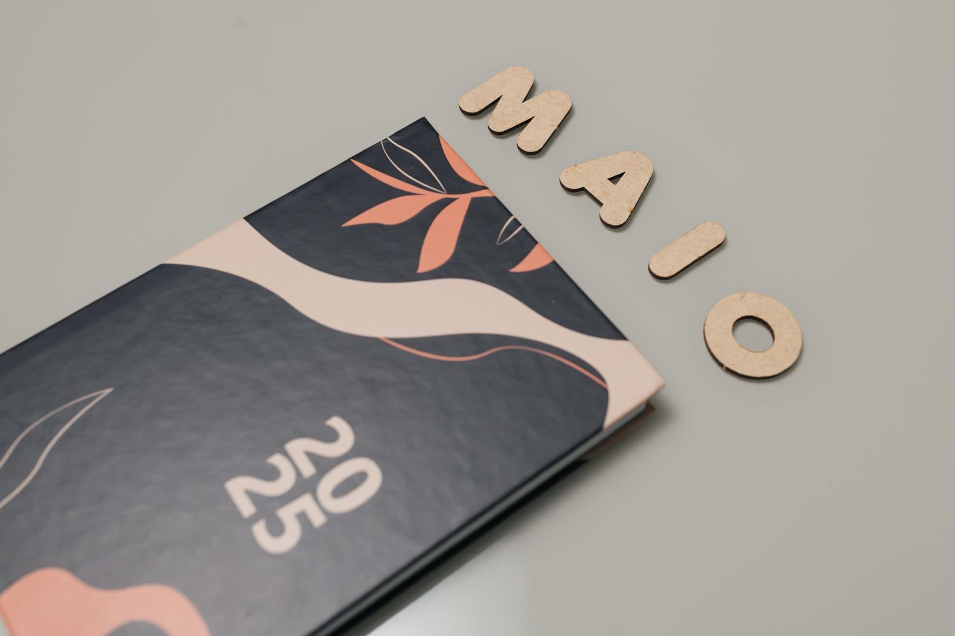 A stylish 2025 planner with modern abstract design next to wooden letters spelling 'MAIO'.