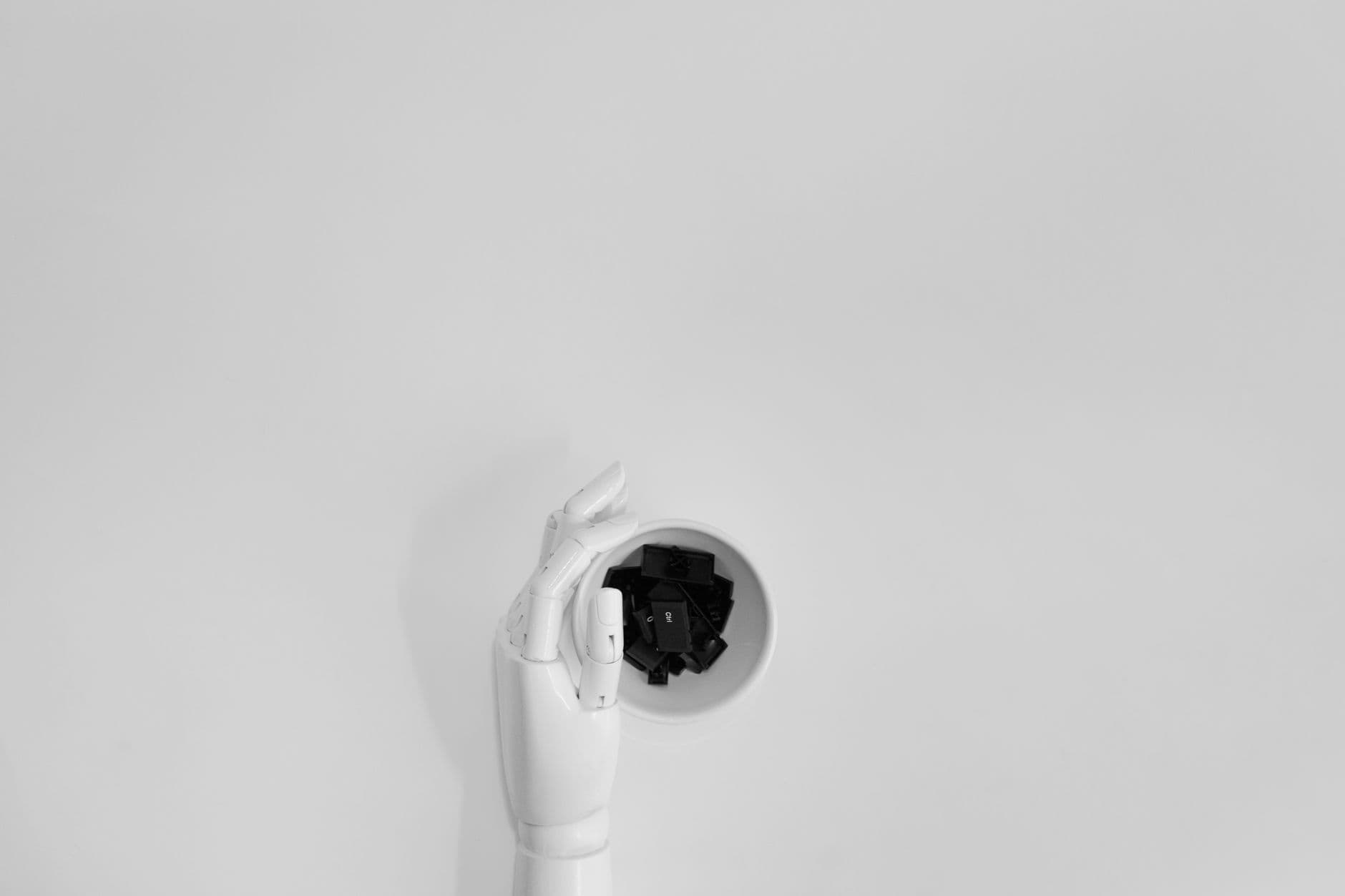 A robotic hand grasping black keyboard keys in a minimalist setting.