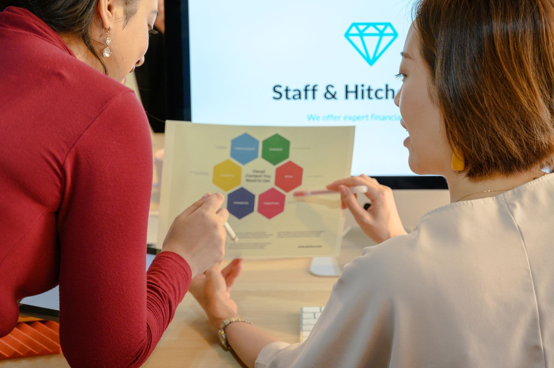 Two women discussing a business project with a color-coded chart in an office setting.
